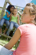 Two young girl friends at a playground whispering about other gi