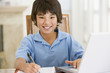 Photo: Young boy with laptop doing homework in dining room smiling Young boy with laptop doing homework in dining room smiling