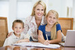 Woman helping two young children with laptop do homework in dini