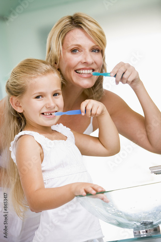 Photo: Woman and young girl in bathroom brushing teeth Woman and young girl in bathroom brushing teeth