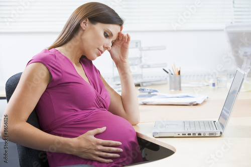 Photo: Pregnant woman at work with laptop looking stressed Pregnant woman at work with laptop looking stressed