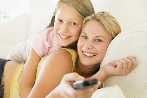 Photo: Woman and young girl with remote control embracing on sofa smili Woman and young girl with remote control embracing on sofa smili