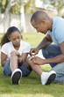 Father applying bandaid to daughter 7-9 in park