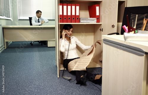 Photo: Office worker on the phone hiding from manager Office worker on the phone hiding from manager