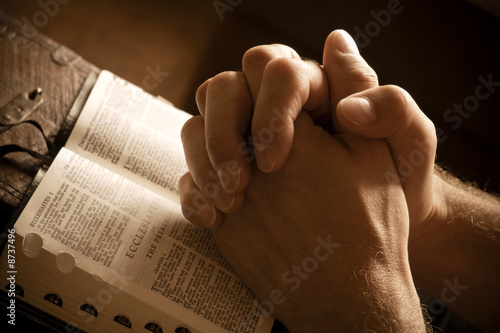 Photo: Praying hands on an open bible Praying hands on an open bible