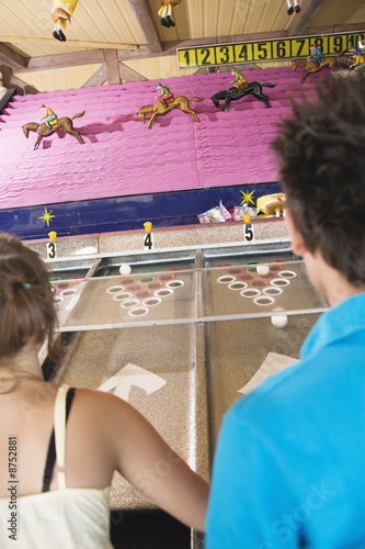 Photo: Teenage couple playing horse racing game in amusement park Teenage couple playing horse racing game in amusement park