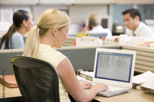 Photo: Businesswoman in cubicle using laptop Businesswoman in cubicle using laptop