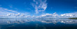 Blue bright summer sky with white clouds reflecting in lake