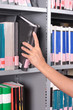 hand removing or replacing a book on a library shelf