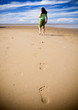 Foto: Young girl walking on the beach leaving footprints in the sand Young girl walking on the beach leaving footprints in the sand