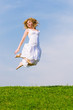 Girl jumps on a green grass on a background of the blue sky