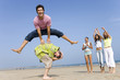 Young man leaping over friend at beach, women cheering