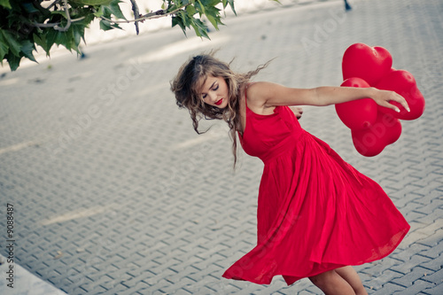 Photo: Beautiful girl in red dress moving with ballons as hearts Beautiful girl in red dress moving with ballons as hearts