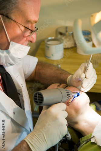 Photo: A mature dentist working on a lady patient using a curing light. A mature dentist working on a lady patient using a curing light.
