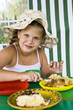 Little girl in big hat eats sweets and drinks tea
