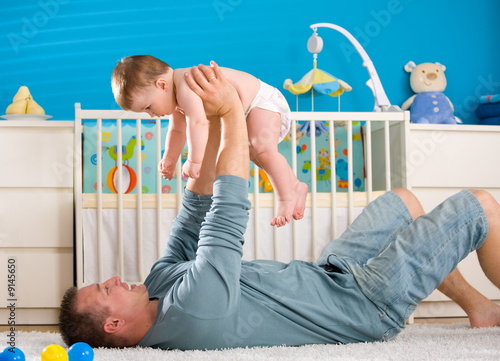 Photo: Father lying on back and lifting baby boy ( 1 year old ) at home Father lying on back and lifting baby boy ( 1 year old ) at home