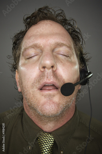 Photo: Businessman Sleeps Wearing a Phone Headset - Grey Background. Businessman Sleeps Wearing a Phone Headset - Grey Background.