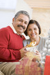 Middle Aged Couple Sitting On Sofa Holding Christmas Present