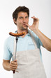 Young man with grilled sausage on fork, portrait