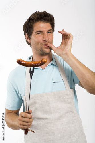 Foto: Young man with grilled sausage on fork, portrait Young man with grilled sausage on fork, portrait