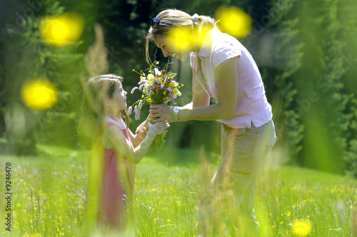 Foto: Mother passing bouquet to daughter (6-7) in meadow, side view Mother passing bouquet to daughter (6-7) in meadow, side view