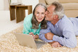 Mature couple lying on carpet with laptop, man kissing woman Mature couple lying on carpet with laptop, man kissing woman