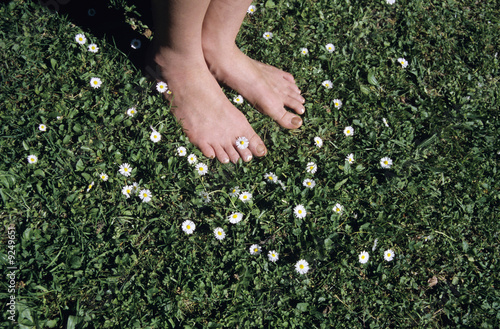 Photo: Feet on grass with daisy flowers, close-up Feet on grass with daisy flowers, close-up