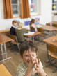 Children (4-7) in class room, focus on boy gesturing in foreground, elevated view