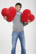 Young man holding heart-shaped cushions, portrait