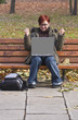 Happy redheaded girl with a laptop in an autumn park.