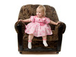 The little girl sits in the big armchair.