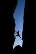 Rock climber silhouetted as he climbs up a chimney .