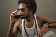 Photo: Portrait of young trendy african man drinking from a glass Portrait of young trendy african man drinking from a glass