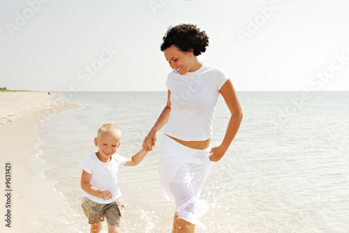 Photo: Happy young mother and male child walking on beach. Happy young mother and male child walking on beach.