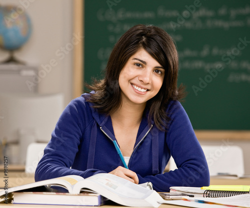 Photo: Student with text books doing homework in school classroom Student with text books doing homework in school classroom