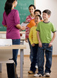Students listen to teacher with clipboard in school classroom
