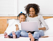 Mother and daughter typing on laptop on bed in bedroom