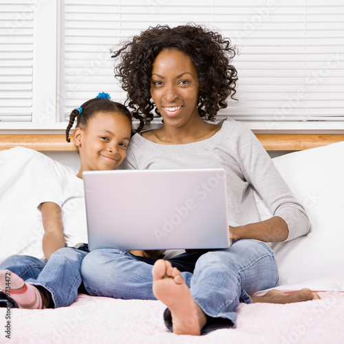 Photo: Mother and daughter typing on laptop on bed in bedroom Mother and daughter typing on laptop on bed in bedroom