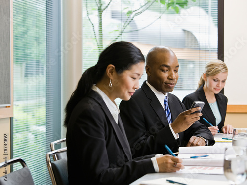 Photo: Businessman with co-workers text messaging on cell phone Businessman with co-workers text messaging on cell phone