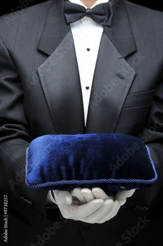 Butler holding a velvet pillow in front of his torso
