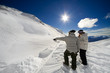 Two snowboarders pointing at and overlooking a jump