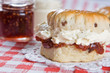 A scone with clotted cream with jam in the background
