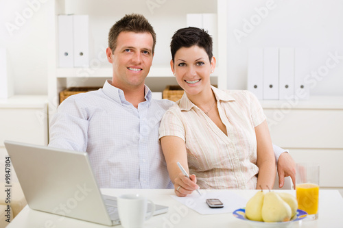 Photo: Couple working on laptop computer at home office, smiling. Couple working on laptop computer at home office, smiling.