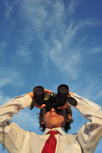 Foto: Young business man looking through binocular, low angle view Young business man looking through binocular, low angle view