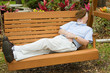 Senior man stretched out on a park swing taking a nap.