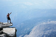 Man standing on top of a cliff with arm raised Man standing on top of a cliff with arm raised