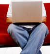 A man sitting on a red couch working on a laptop computer