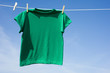 A green t-shirt hanging on a clothesline in front of a blue sky