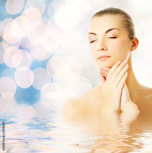 Beautiful young woman in water massaging her face