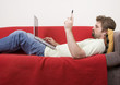 young man is lying on the sofa and works on the laptop